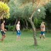 Quattro persone giocano a pallavolo su un prato, circondato da alberi.