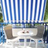 Due sedie e un tavolino bianco su un balcone con tenda a righe blu.