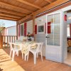 Veranda in legno, tavolo con sedie bianche, porta aperta.