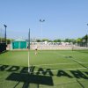 Campo da tennis in erba sintetica con una persona che gioca, sotto il cielo blu.