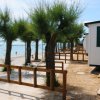 Spiaggia sabbiosa con alberi, bungalow bianchi e staccionata in legno.