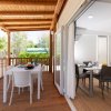 Veranda in legno con tavoli e sedie, affacciata su un giardino verde.