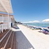 Spiaggia con sedie a sdraio e ombrelloni, accanto a una terrazza in legno.