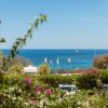 Vista sul mare con bandiere e vegetazione.