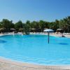 Piscina circolare con ombrelloni e lettini bianchi. Alberi verdi sullo sfondo.