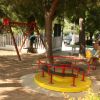 Un parco giochi con altalene, una giostra gialla e bambini che giocano tra gli alberi.
