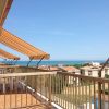 Terrazza con tende da sole arancioni e vista sul mare e case in lontananza.