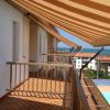 Balcone con tende da sole arancioni e vista su piscina, palazzi e mare.