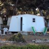 Casetta bianca con sedie a sdraio verdi e tavolo, immersa tra gli alberi.