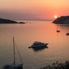 Tramonto su una baia con barche e yacht su acque calme, cielo arancione e sole vicino all'orizzonte.