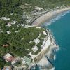 Vista aerea di una costa con spiaggia, mare azzurro e densa vegetazione.