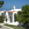 Villa bianca con tetto in tegole rosse, circondata da pini, vista sul mare.