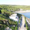 Veduta aerea di un edificio bianco sulla costa circondato da vegetazione e mare.