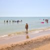 Spiaggia soleggiata con persone che nuotano e camminano vicino alla riva.