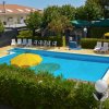 Piscina all'aperto con lettini e ombrelloni gialli, circondata da alberi e siepi.
