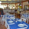 Interno di ristorante con tavoli apparecchiati, sedie in plastica, e vetrina sullo sfondo.