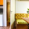 Interno di un bungalow con divano a motivi gialli, tavolo, pianta e cucina con frigorifero.