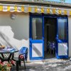 Esterno di una casa con porte blu, tavolo e sedie da giardino, giochi per bambini sul pavimento.