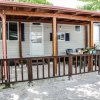 Veranda in legno con tavolo e sedie, circondata da un parapetto e alberi.