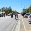 Persone in bicicletta lungo una strada con auto parcheggiate e alberi ai lati.