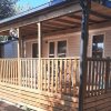Una casa mobile con una veranda in legno ombreggiata e recintata.