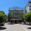 Facciata di un hotel con palme e tavolini all'aperto.