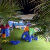 Un parco giochi con scivolo colorato e giochi in plastica su un prato verde circondato da palme.
