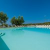 Piscina con gradini, circondata da lettini e ulivi, sotto un cielo sereno.