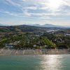 Panorama aereo di una costa con ombrelloni, resort e campagna collinare sullo sfondo.