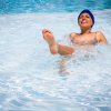 Persona in piscina con cuffia blu e sorriso mentre gioca nell'acqua.