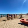 Persone che ballano sulla spiaggia in un giorno soleggiato. Il mare è visibile a sinistra.