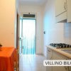 Cucina con tavolo arancione e ingresso con porta trasparente. Scritta: 