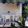 Veranda con tavolo bianco e sedie in plastica, coperta da un tendone verde, circondata da piante.