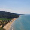 Lunga spiaggia sabbiosa con mare azzurro e colline verdi.