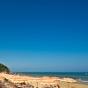 Spiaggia soleggiata con file di ombrelloni gialli e arancioni, mare calmo.