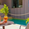 Persona seduta all'aperto, tiene un drink vicino a una piscina e piante verdi.