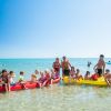 Gruppo di persone su pedalò in mare poco profondo con cielo sereno.