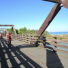 Ciclisti su un ponte di legno costiero con vista sul mare.