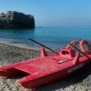 Spiaggia con pedalò rosso sulla sabbia. Sfondo di mare calmo e scoglio.