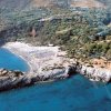 Spiaggia con ombrelloni colorati vista dall'alto, circondata da rocce e vegetazione.