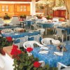 Ristorante all'aperto con tavoli apparecchiati con tovaglie blu, fiori rossi attorno.