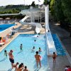 Piscina con scivoli d'acqua, persone che nuotano e si rilassano al sole.