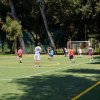 Un gruppo di persone gioca a calcio su un campo all'aperto circondato da alberi.