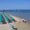 Spiaggia con file di ombrelloni verdi e persone che nuotano nel mare.