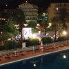 Piscina notturna illuminata con palme e edifici vicini.