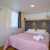 Letto con copriletto rosa, finestra con tende bianche e nere.