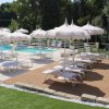 Piscina con lettini e ombrelloni bianchi su terrazza in legno.