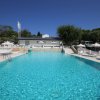 Piscina azzurra con lettini e ombrelloni bianchi, cielo limpido.