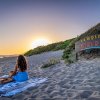Tramonto su spiaggia con donna e cartello camping.