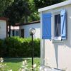 Una casa mobile con persiane blu aperte e un prato verde.